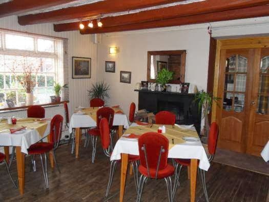 Cozy bar interior with red chairs, white tables, wooden beams, plants, and a fireplace in Ottringham, Yorkshire.