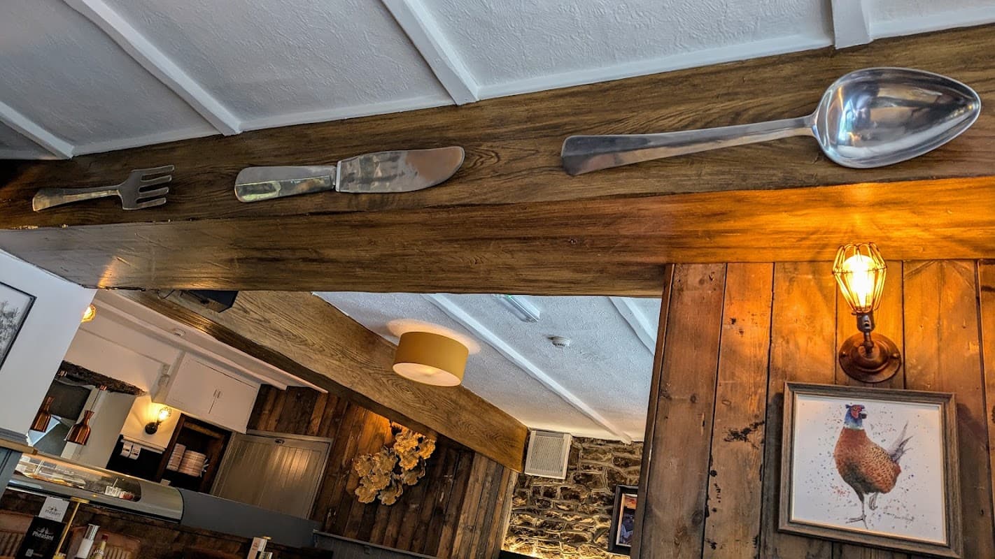 Decorative fork, knife, and spoon mounted on wooden beams; warm lighting and rustic decor in a cozy restaurant setting.