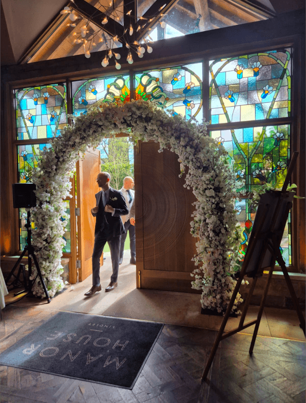 Elegant floral archway at The Petal Studio entrance, with stained glass windows and a stylish interior.
