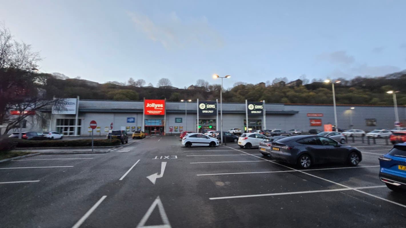 Car park with multiple vehicles, shops in the background, and clear exit signage in Ovenden, Yorkshire.