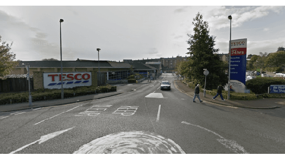 Car park entrance near Tesco in Ovenden, Yorkshire, with cars and pedestrians visible on the road.