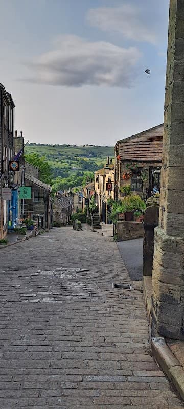 Cobblestone street lined with stone buildings, greenery, and hills in the background, capturing a serene Yorkshire village scene.