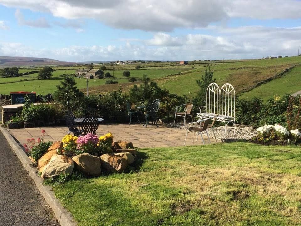 Scenic garden patio with seating, flowers, and rolling green hills under a partly cloudy sky at Leeming Wells Hotel.