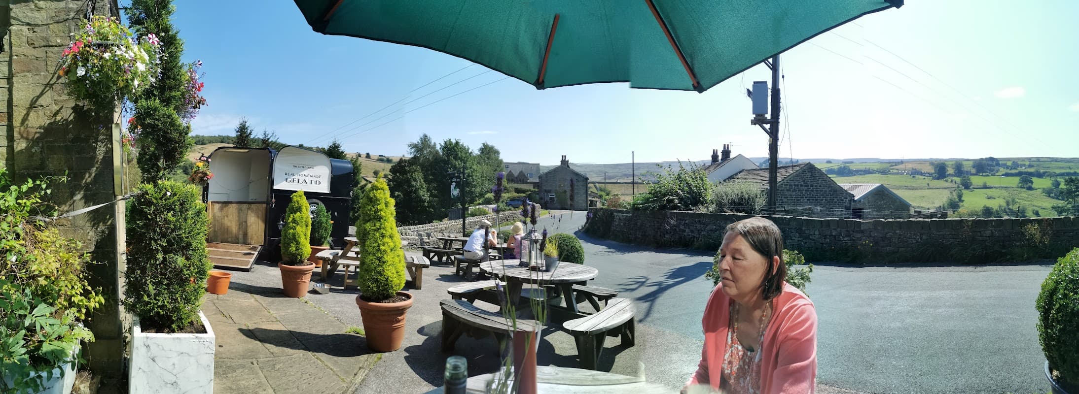 The Lamb Inn features outdoor seating, lush greenery, and a scenic view of the Yorkshire countryside under a large umbrella.
