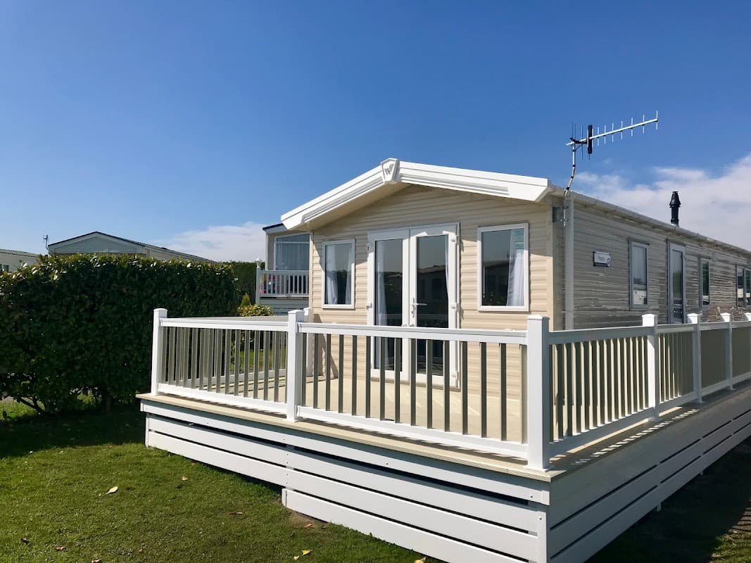 Modern holiday home with a deck, surrounded by green hedges and a clear blue sky at Upwood Holiday Park, Oxenhope.