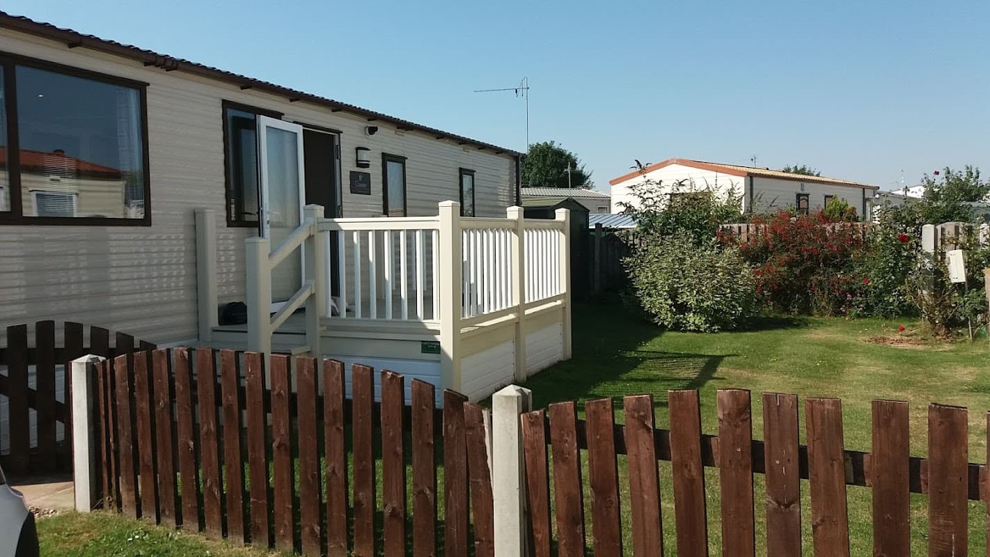 A holiday home with a white railing, surrounded by a grassy area and wooden fence, under a clear blue sky.