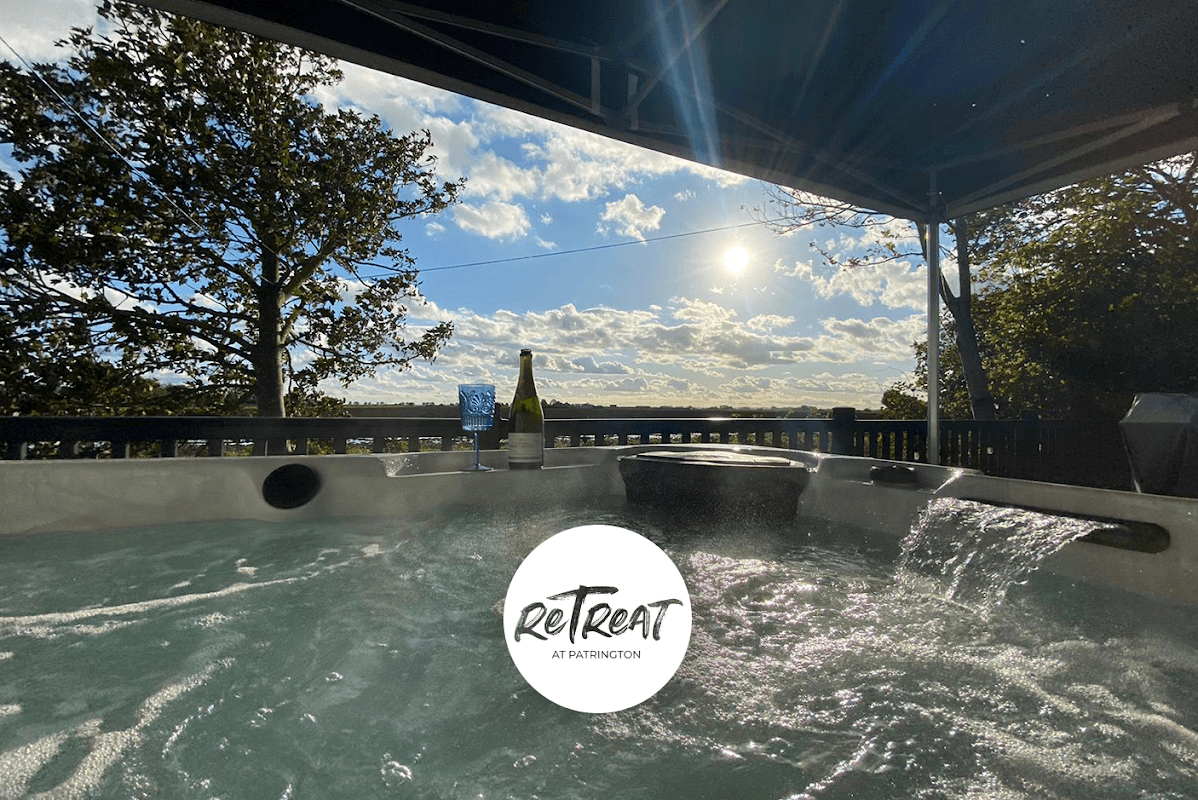 Hot tub with a scenic view of the sky and trees, featuring a bottle of champagne and glasses nearby.