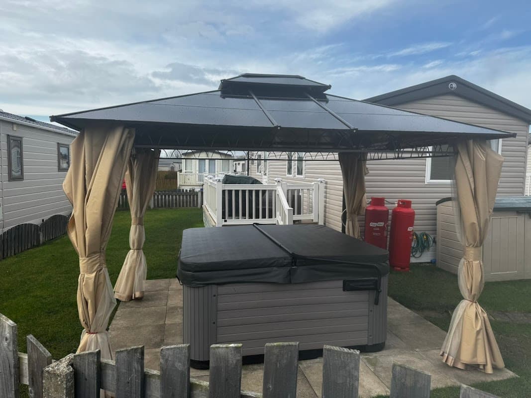 Hot tub under a gazebo with curtains, surrounded by holiday homes and a grassy area in Patrington, Yorkshire.