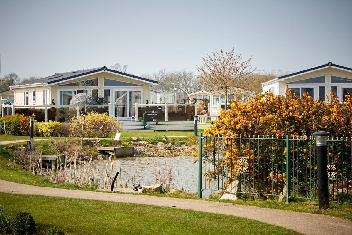 Colorful holiday lodges by a serene pond, surrounded by greenery and blooming flowers at Patrington Haven Leisure Park.