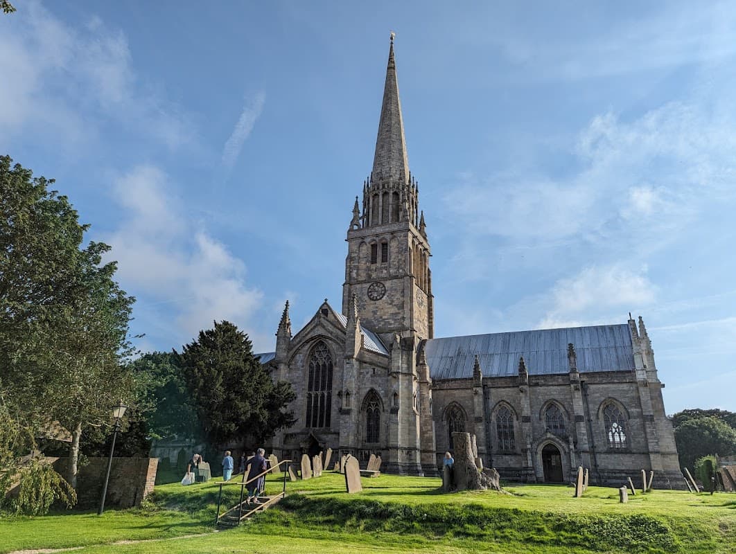 St Patrick's Church features a tall spire, stone architecture, and surrounding greenery with gravestones in the foreground.