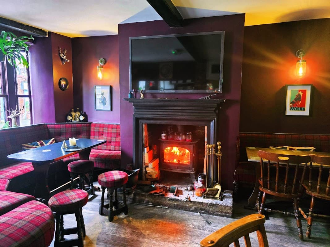 Cozy bar interior with plaid seating, a fireplace, and a large TV on a purple wall, creating a warm atmosphere.