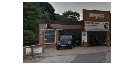 Penistone Tyres Limited garage with a black vehicle parked outside and signage displaying contact information.