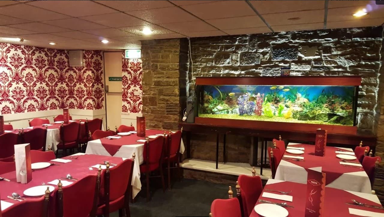 Elegant dining area with red tablecloths, ornate wallpaper, and a large aquarium as a focal point.