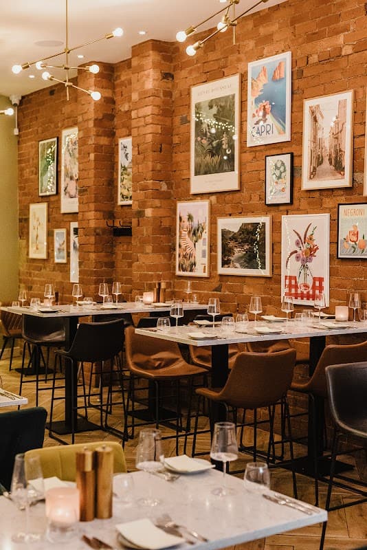 Warm brick walls adorned with colorful artwork, elegant tables set with glasses, and soft lighting create a cozy ambiance.