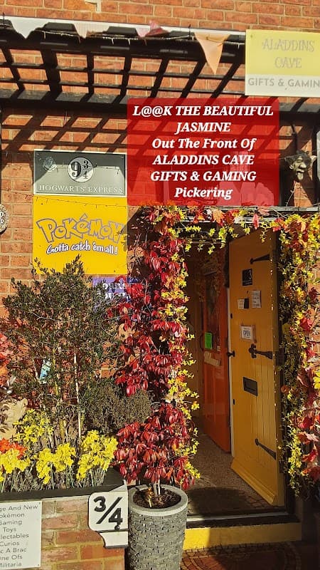 Colorful storefront of Aladdin's Cave Gifts & Gaming, adorned with flowers and signs, in Pickering, Yorkshire.
