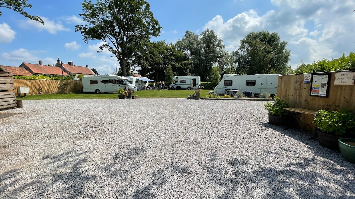 Gravel parking area with caravans, green trees, and blue sky at Lakeside Caravan Park in Pickering, Yorkshire.