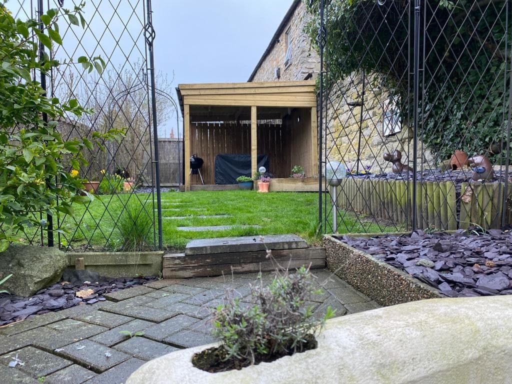Quaint garden with green lawn, wooden pergola, stone walls, and decorative plants in Lavender Cottage, Pickering.