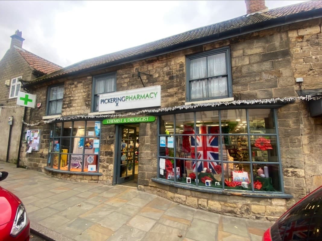Stone building with large windows, displaying festive decorations and a Union Jack flag, labeled "Pickering Pharmacy."