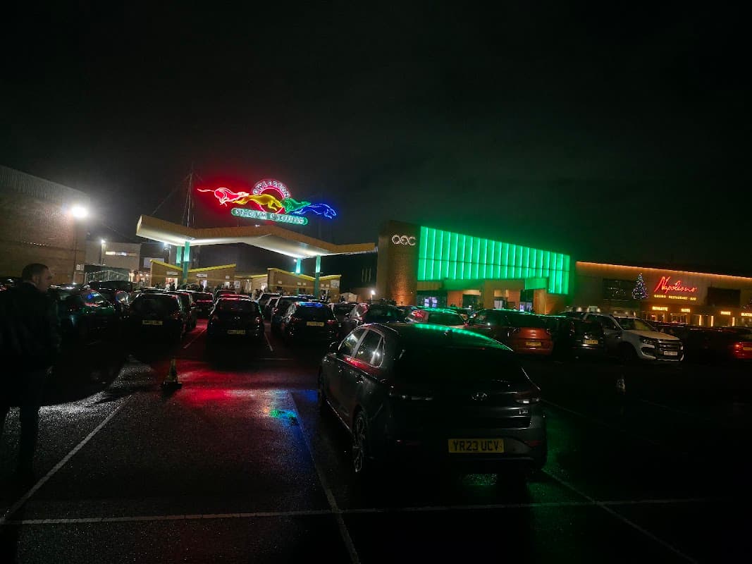 Brightly lit "Box of Dreams" sign with colorful neon, busy parking lot, and modern buildings under a night sky.