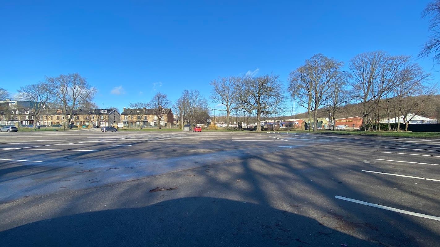 Spacious car park with empty parking spaces, surrounded by trees and buildings under a clear blue sky.