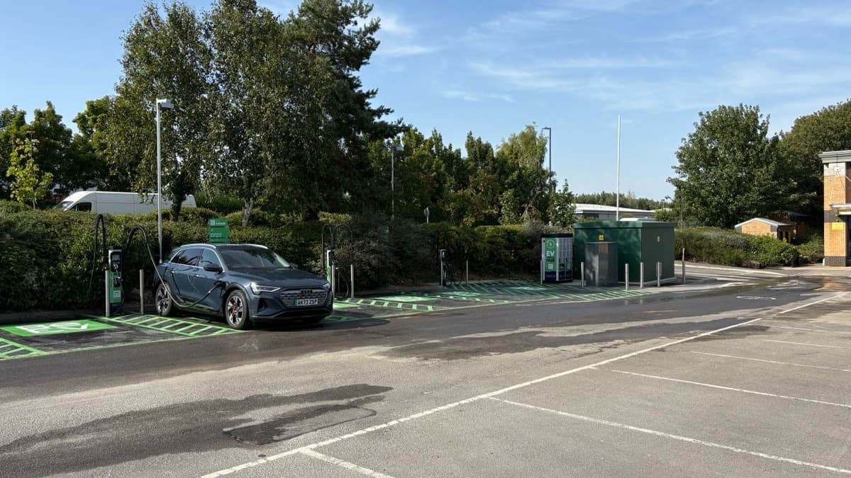 Be.EV Charging Station with electric vehicle parked, green charging spots, and trees in the background.