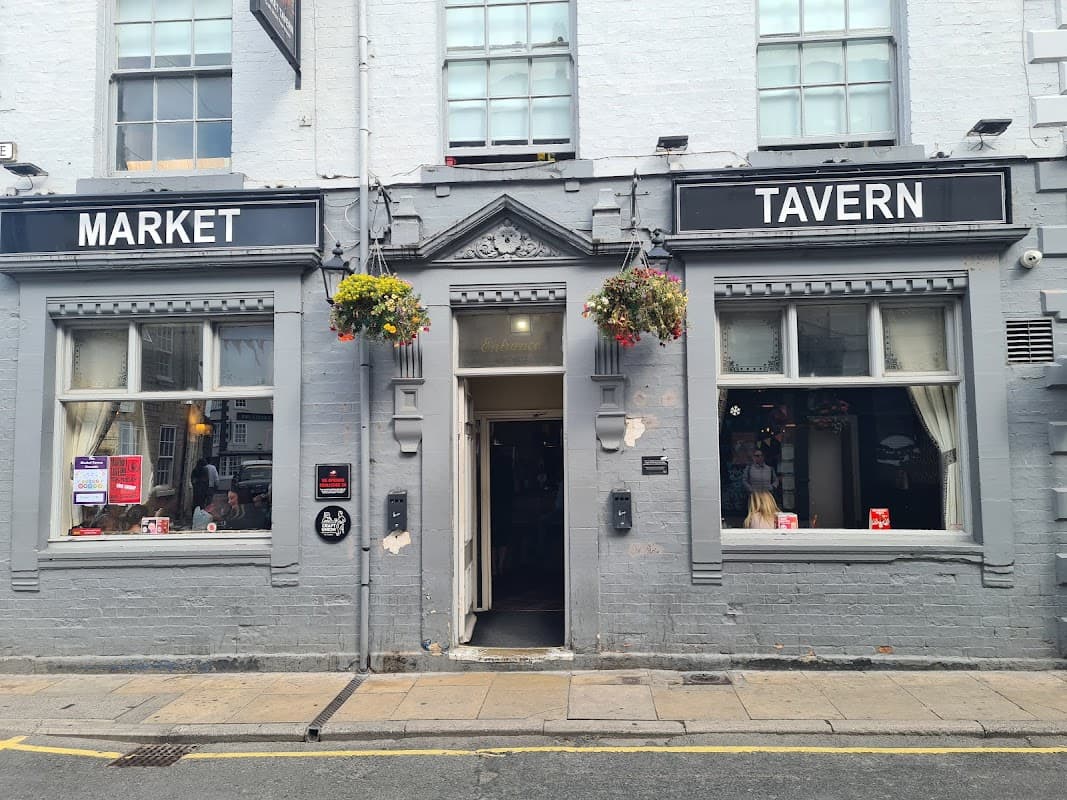 Exterior of Market Tavern, a bar in Plompton, Yorkshire, featuring hanging flower baskets and large windows.