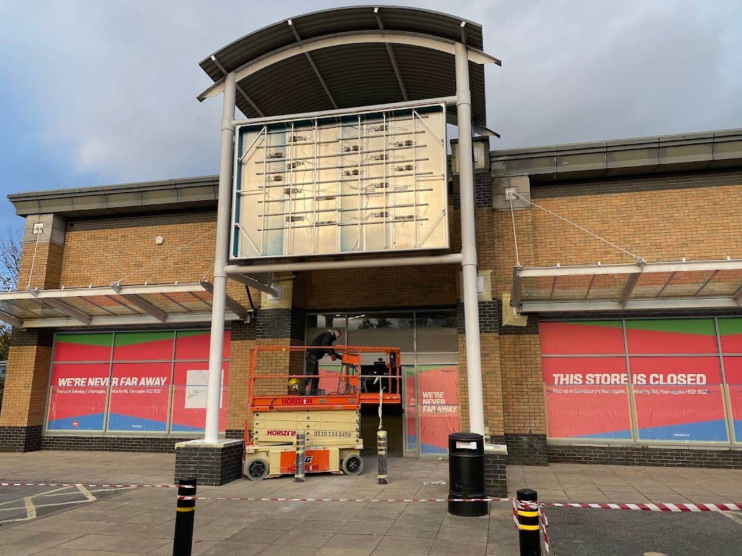 Closed storefront with colorful signage; a worker on a lift is making repairs outside.