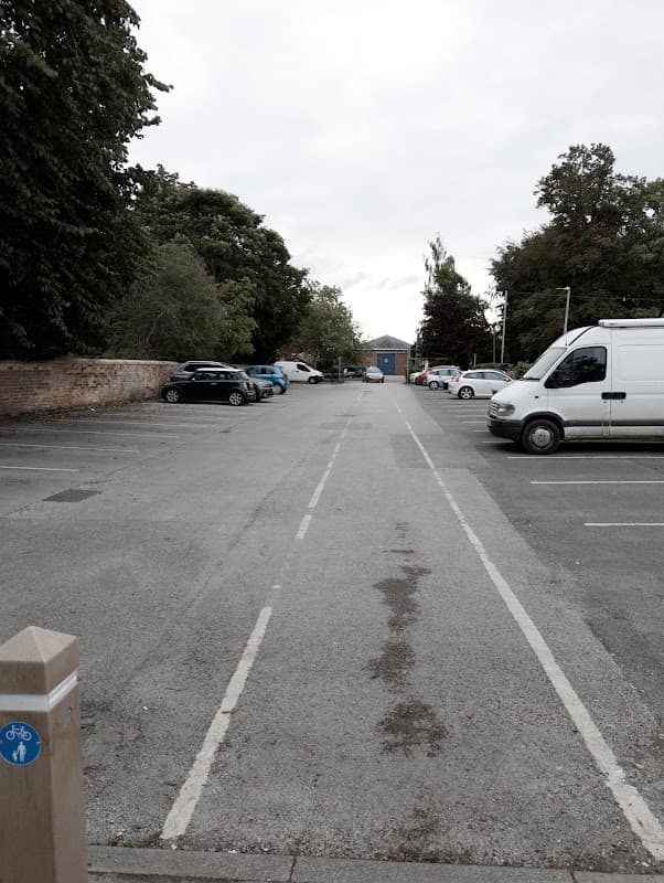 Free parking lot in Pocklington, Yorkshire, with parked cars, trees, and a building in the background under a cloudy sky.