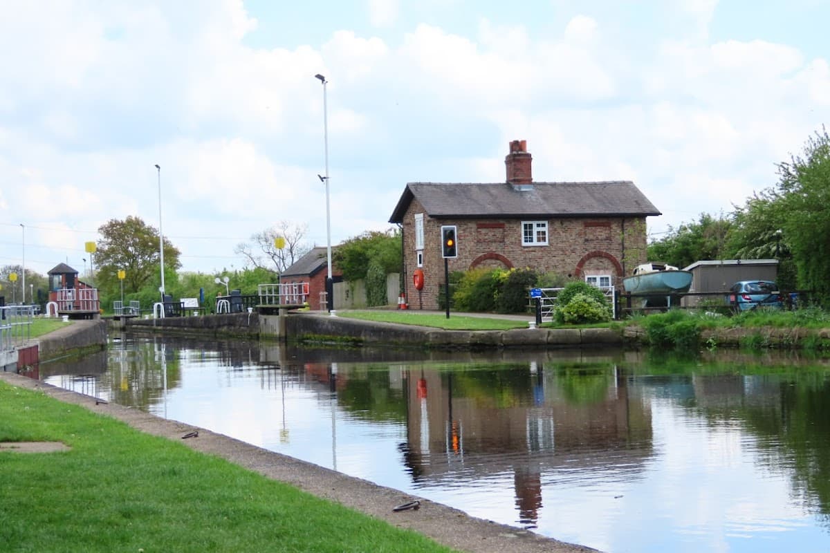 Pollington Village Hall beside a calm canal, surrounded by greenery and blue sky with fluffy clouds.