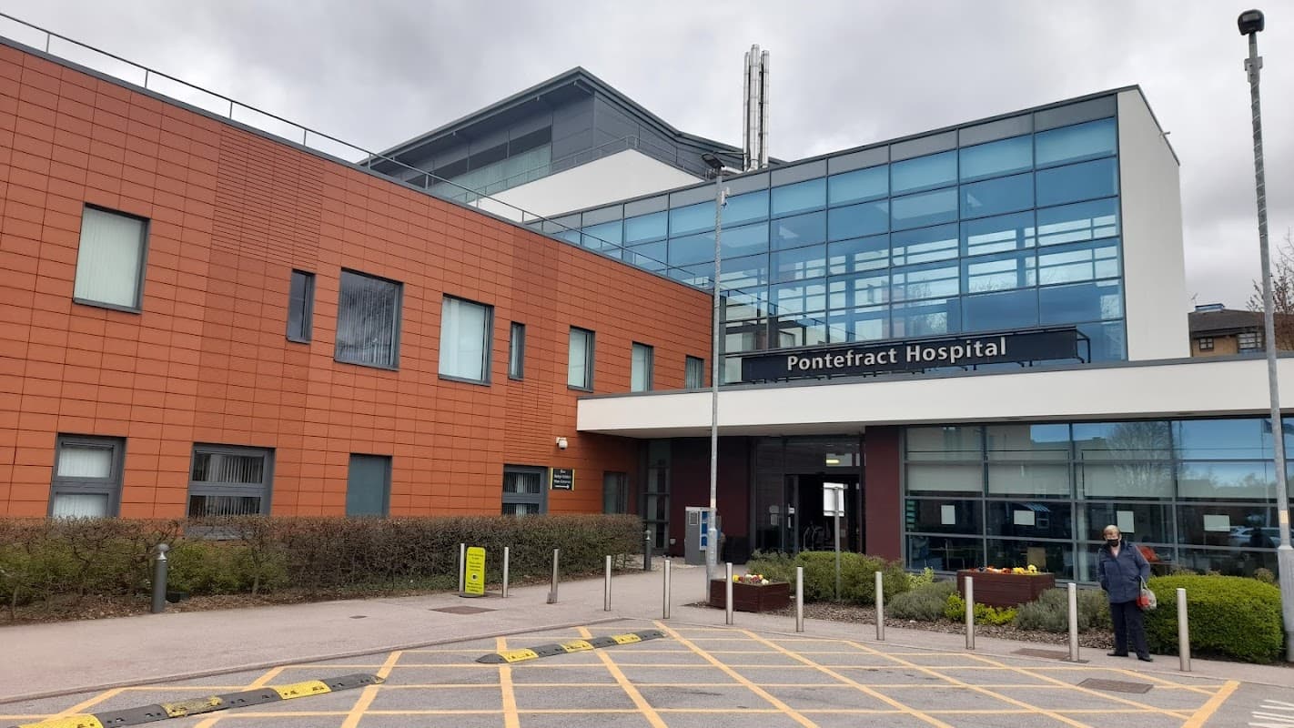 Modern hospital building with large glass entrance, red brick facade, and landscaped pathway in front.