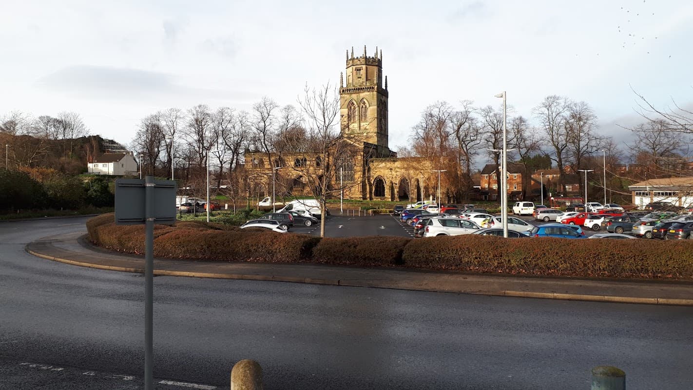 Pay & Display car park with trees, church tower, and various parked cars under a cloudy sky in Pontefract, Yorkshire.