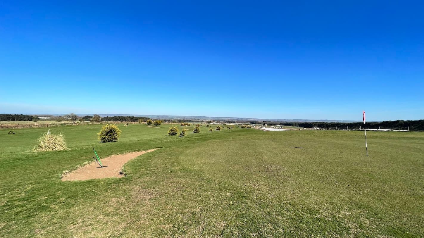 Vast green golf course with neatly trimmed grass, scattered trees, and a clear blue sky in Potter Brompton, Yorkshire.