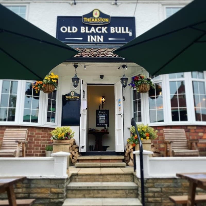 Charming pub entrance with green awnings, flower baskets, and wooden seating in Raskelf, Yorkshire.