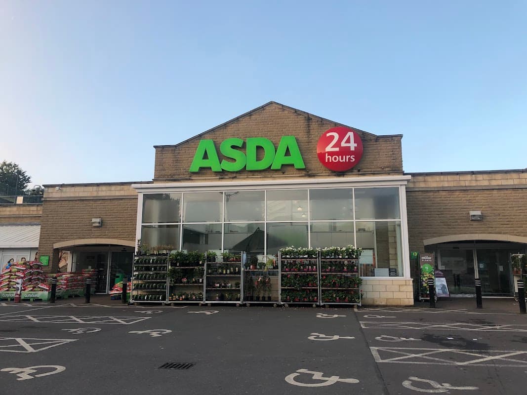 ASDA superstore entrance with large green signage, 24-hour indicator, and plant displays outside.