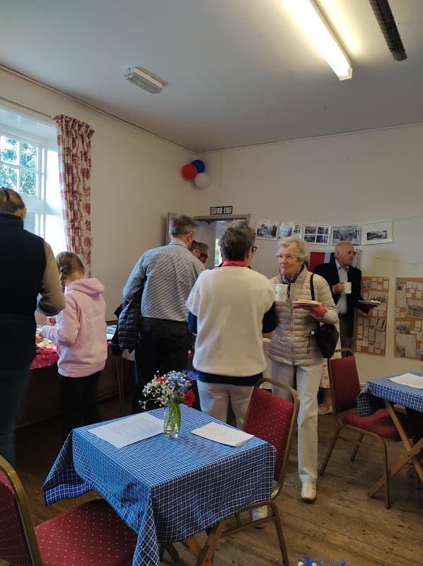 People interacting in a community room with tables, floral arrangements, and historical photos on the walls.