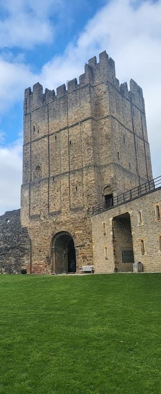 Historic stone tower with battlements, surrounded by green grass and under a partly cloudy sky.