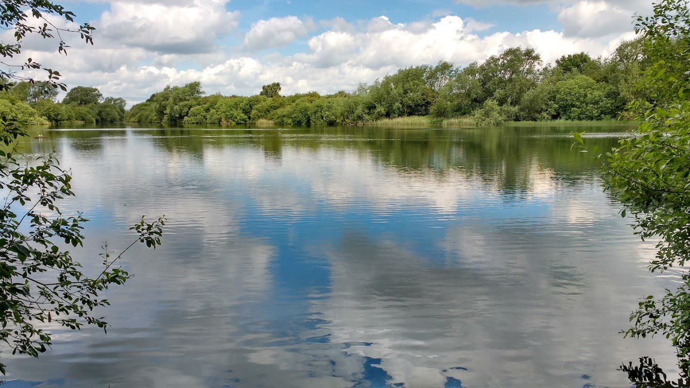 Serene lake reflecting clouds and greenery at Oakhill Nature Reserve, surrounded by lush trees and tranquil waters.
