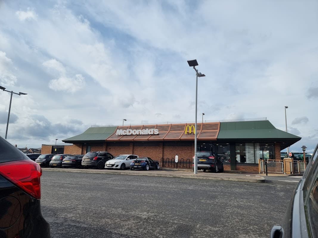 McDonald's restaurant with a green roof, large sign, and parked cars in front under a cloudy sky.