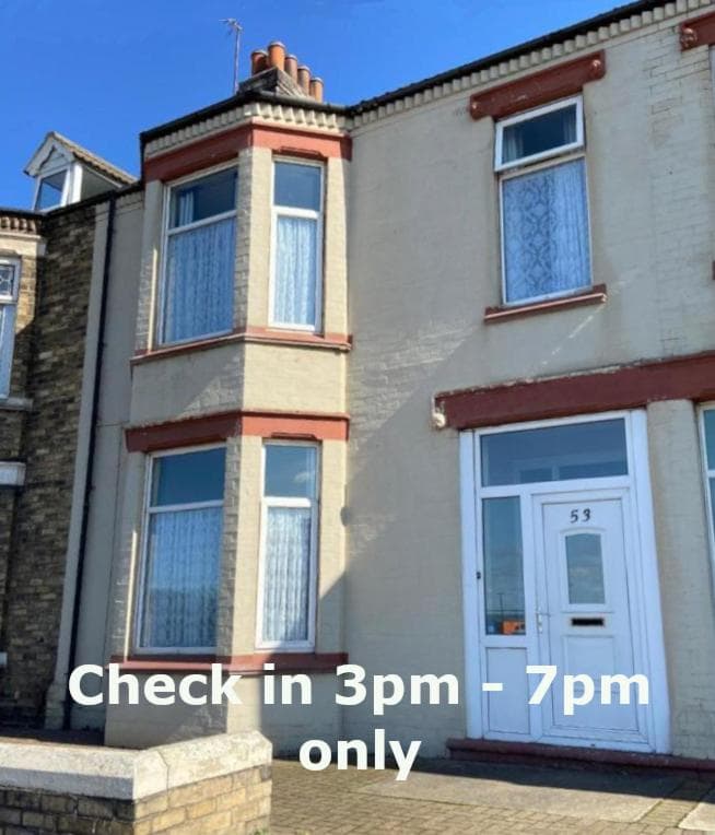 Victorian-style hotel exterior with large windows, a door labeled "53," and a sign detailing check-in hours.