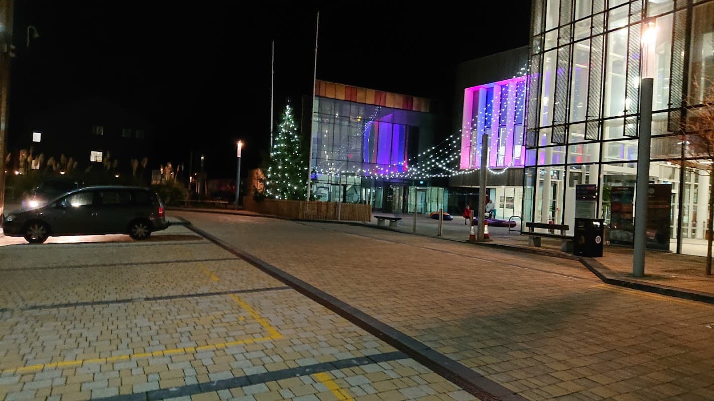Pay & Display car park at night, featuring festive lights and a decorated tree near a modern building.
