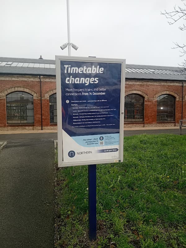 Sign announcing timetable changes for trains, with grassy area and brick building in the background.