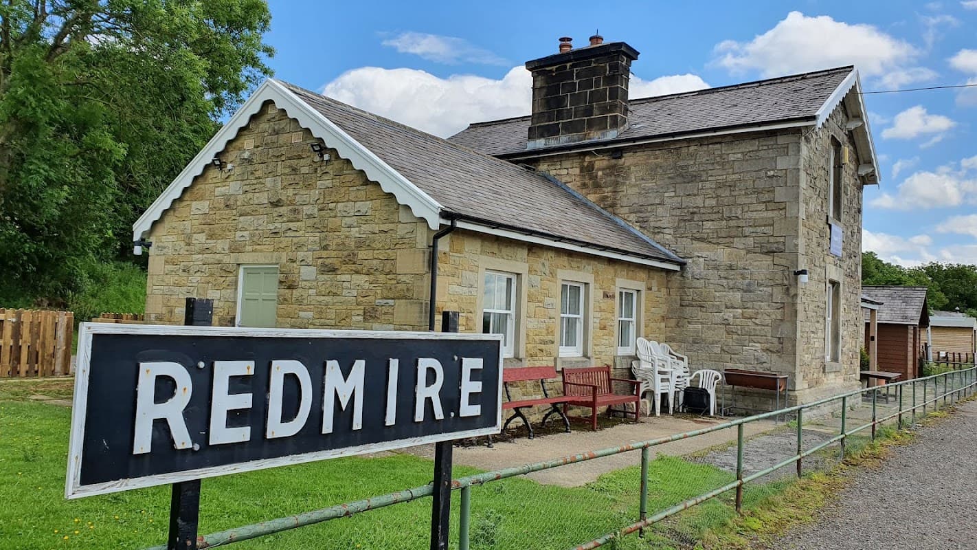 Historic stone building with a slate roof, surrounded by greenery, featuring a sign that reads "REDMIRE."