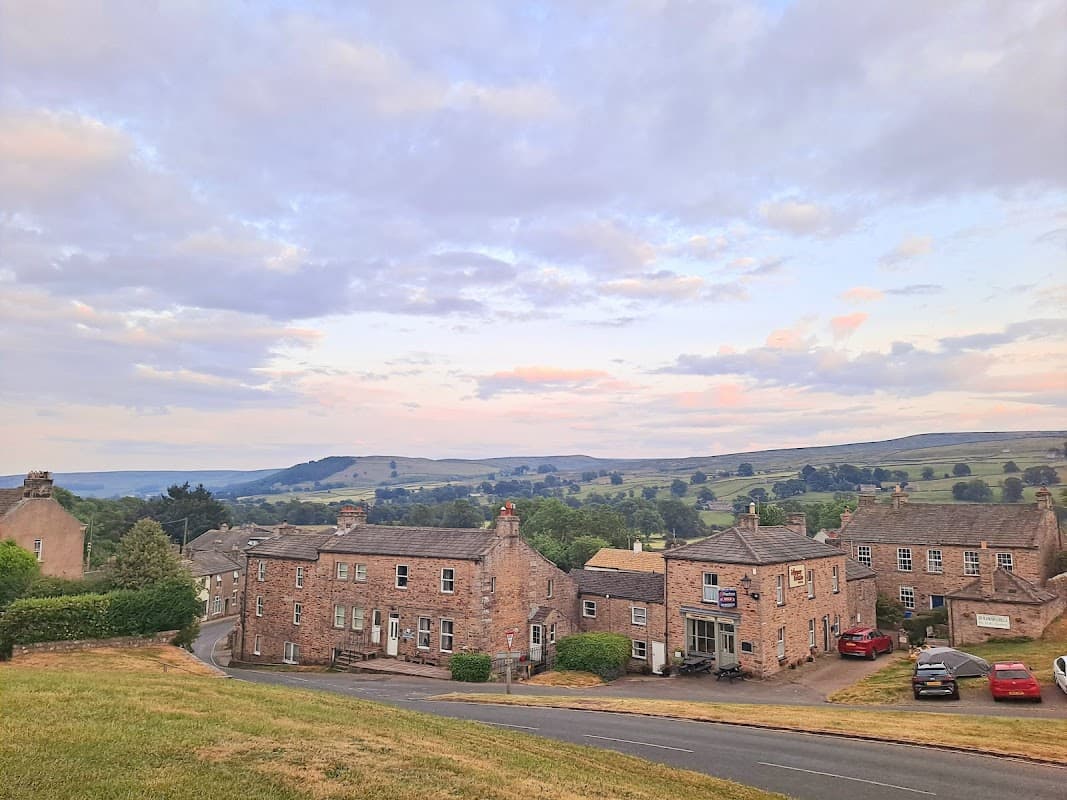 Arkleside Country Guest House with stone facade, surrounded by green hills and a cloudy sky in Reeth, Yorkshire.