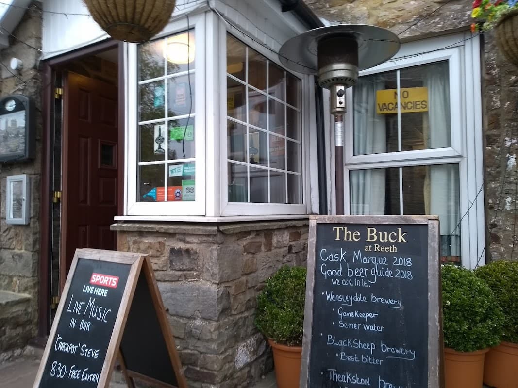 The Buck bar entrance with outdoor seating, menu board, and signs for live music and local breweries.