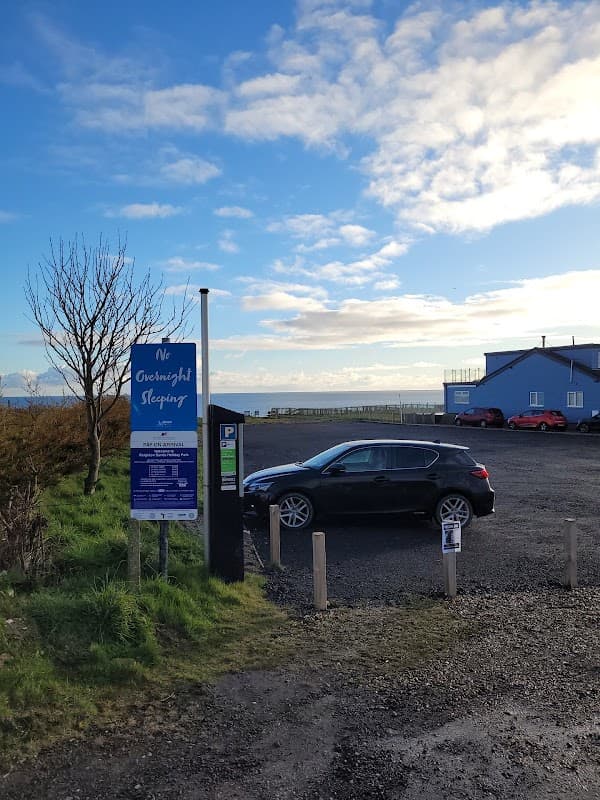 Pay & Display car park at Reighton Sands, featuring a parked car, sign, and a view of the sea in the background.