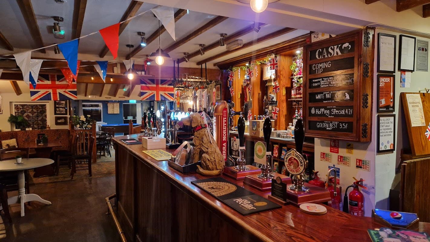 Bar interior featuring a wooden counter, beer taps, Union Jack decorations, and festive bunting.