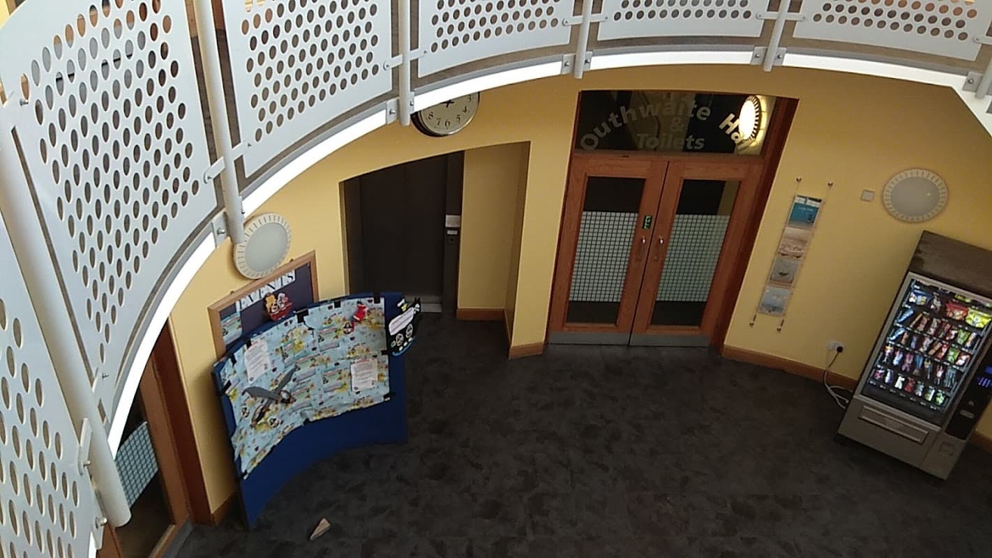 Circular balcony view of The Regen Centre entrance, featuring a map display, vending machine, and clock on the wall.