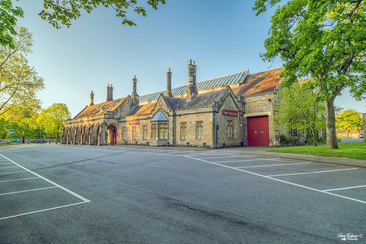 Historic stone building with a red door, surrounded by trees and a parking lot in Richmond, Yorkshire.