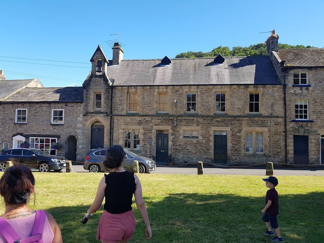Historic stone buildings with slate roofs, grassy area in front, and people walking nearby in Yorke Square, Richmond.