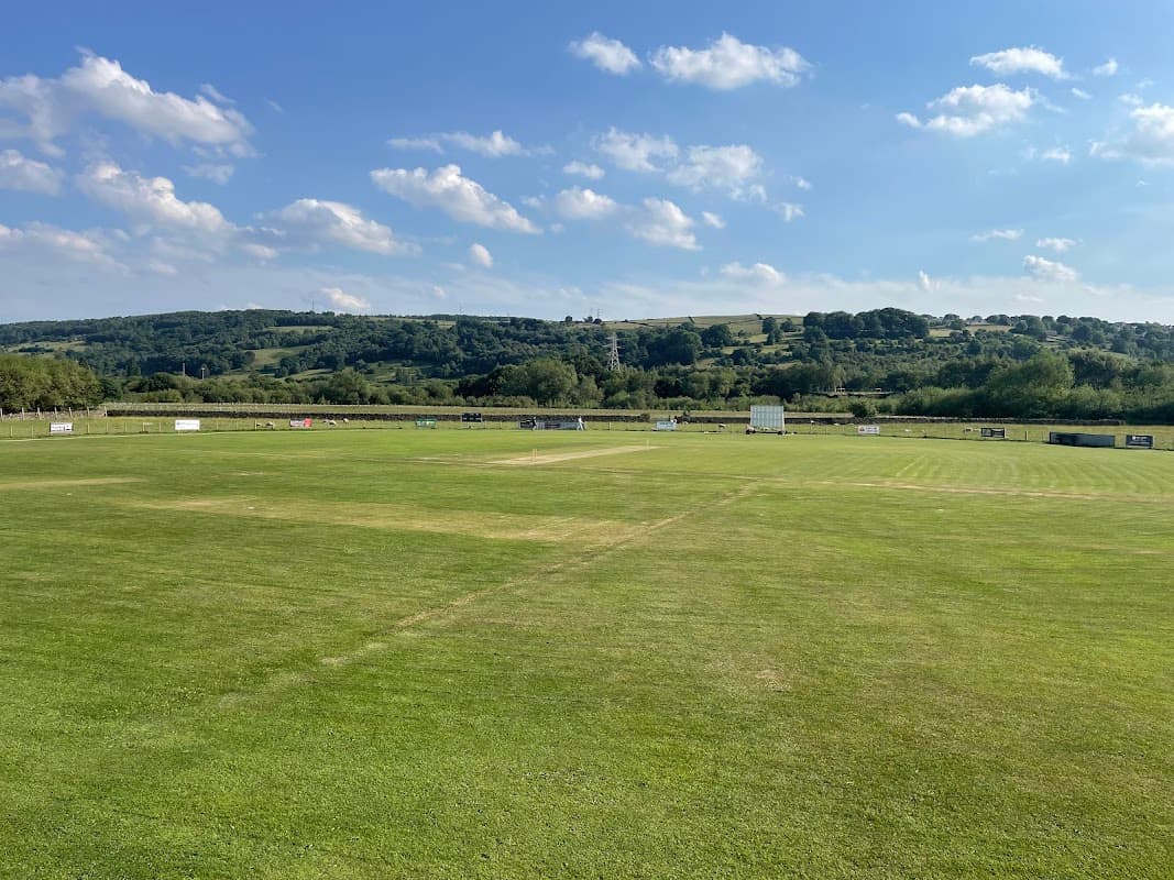 Lush green cricket pitch with a clear blue sky and rolling hills in the background at Airedale Cricket Club.